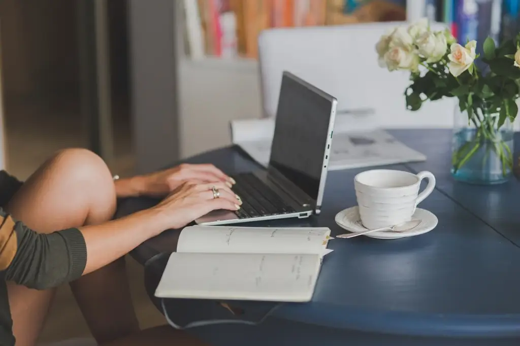 Laptop and coffee cup on a wooden desk with a notepad for tracking metrics